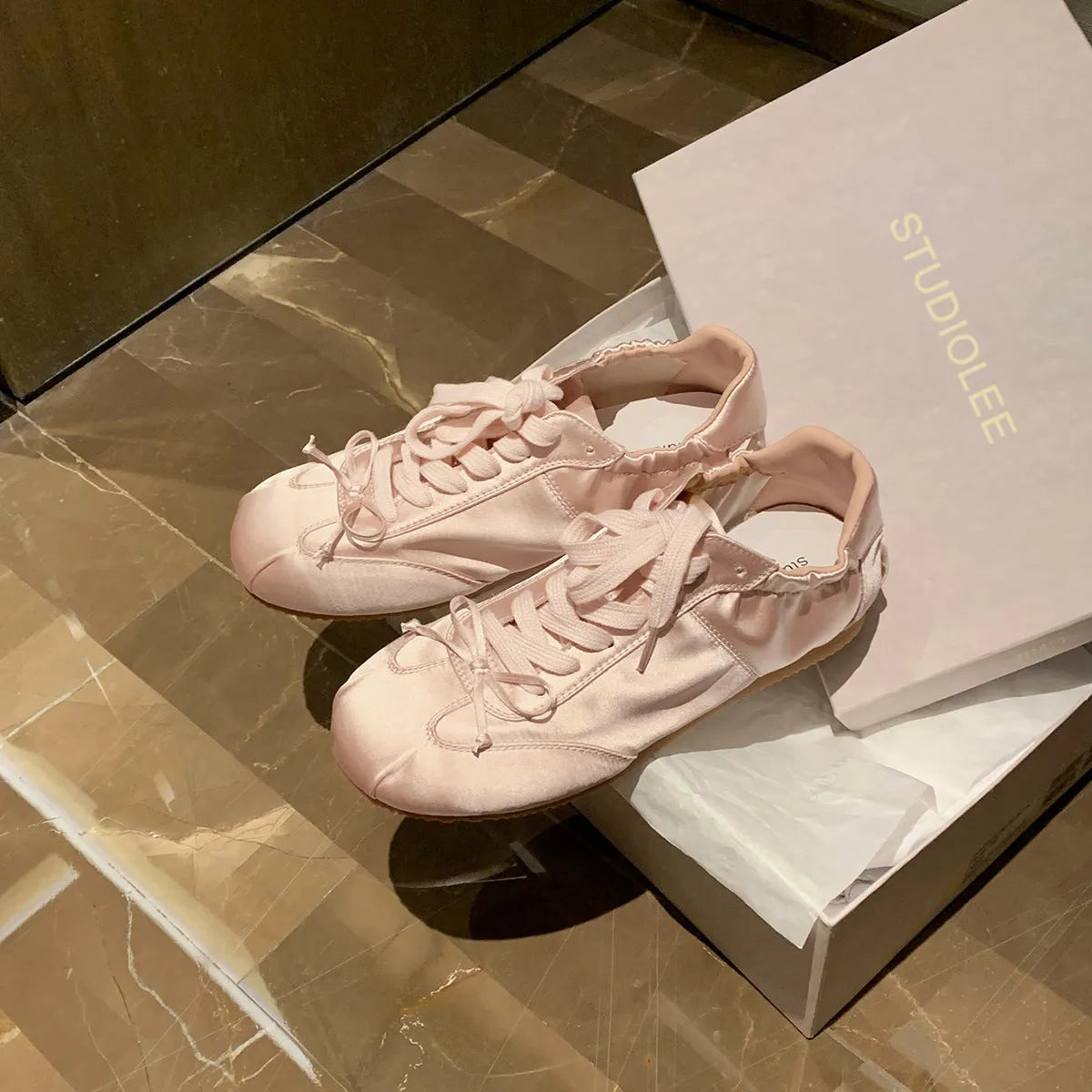 Women's champagne pink satin ballet flats with front lace-up and round toe on a white background.