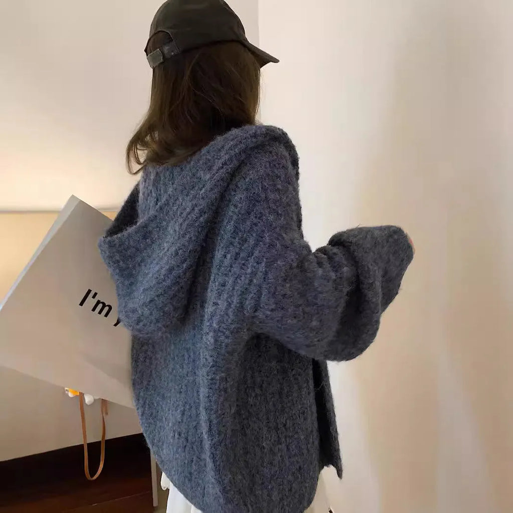 A woman wearing a loose-fit dark grey hooded cardigan made from thick acrylic blend fabric.