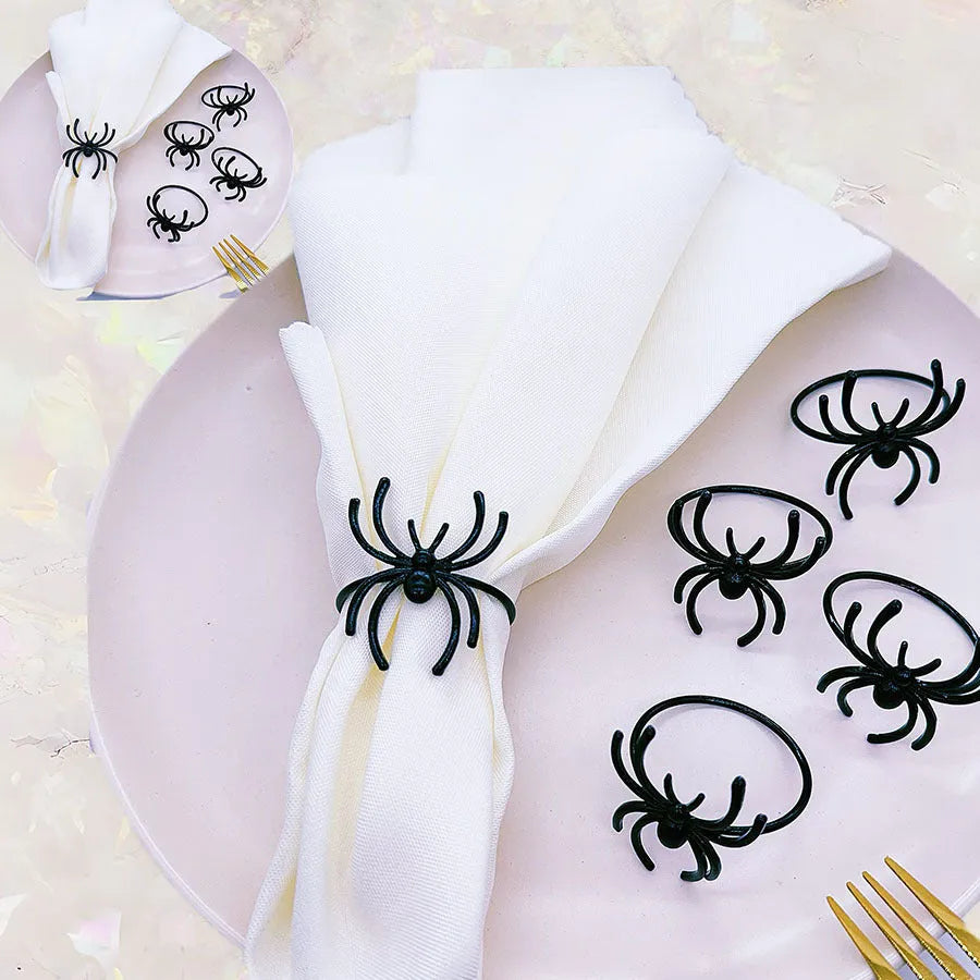 Six black alloy spider-shaped napkin rings on a dark table, showing detailed legs and a 5cm height.